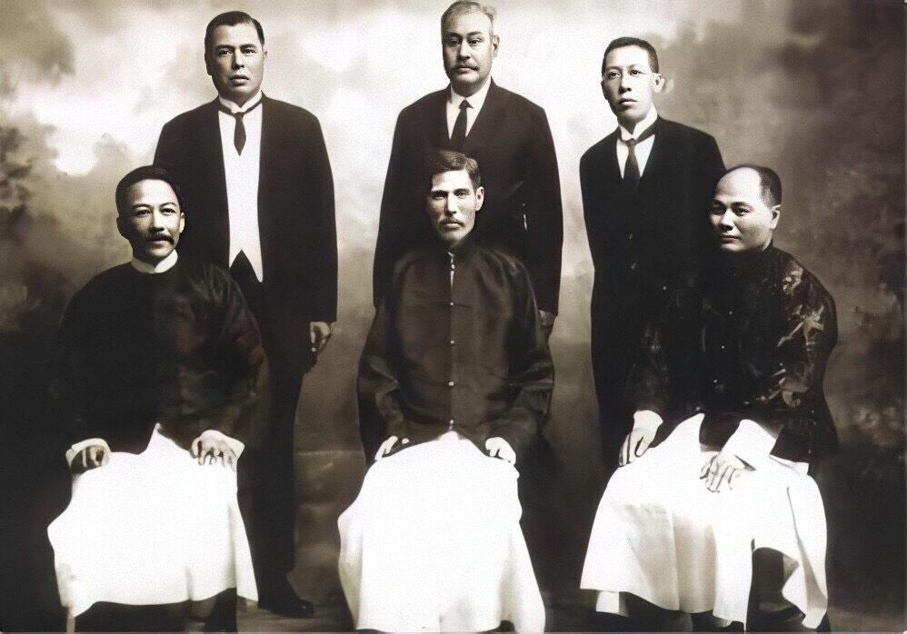 Three men in a formal group portrait, two seated and one standing, early 1920s.